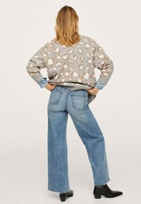 Maglione a stampa leopardata in grigio chiaro e beige, abbinato a jeans a gamba larga blu chiaro. Stivaletti neri alla caviglia e maniche di jeans arrotolate.