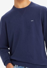 Marinblå bomullströja med ribbad rund halsringning och långa ärmar. Har en liten vit Levi's-logotyp på bröstet. Slät textur.