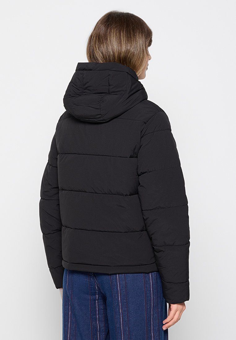 Doudoune noire avec capuche, présentant un design matelassé et des coutures horizontales. Texture douce et isolée pour la chaleur.
