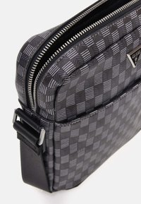 Borsa a scacchi nera e grigia con superficie texturizzata, chiusura con zip e tracolla regolabile. Presenta un accento logo argentato sulla parte anteriore.