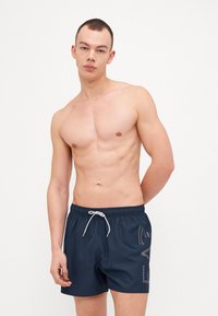 Shorts de bain navy en matériau léger ; taille élastique avec cordon de serrage et détail de logo contrastant sur le côté gauche.