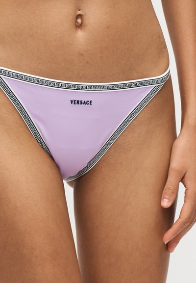 Partie inférieure du torse d'une femme portant un bas de bikini Versace violet clair avec une bordure noire motif clé grecque et un logo centré sur le devant.
