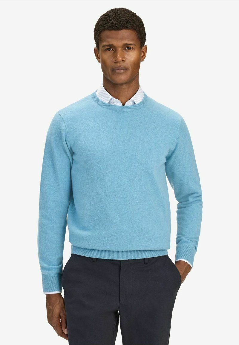 Ljusblå sweatshirt med rund halsringning, tillverkad av mjukt material, med ribbade ärmslut och nederkant, tillsammans med en vit skjorta med krage under.