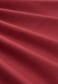 Miękka, gładka tkanina w głębokim różowym kolorze z delikatnymi fałdami tworzącymi subtelne cienie i fakturę na powierzchni.