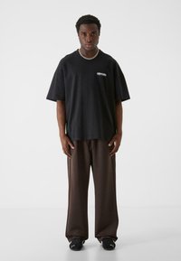 Sort oversized t-shirt med et lille hvidt logo på brystet, parret med brune løstsiddende bukser og sorte sneakers.