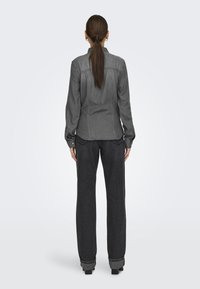 Camisa de mezclilla gris de manga larga con un dobladillo ligeramente curvado, combinada con pantalones anchos de un gris oscuro con puños enrollados.