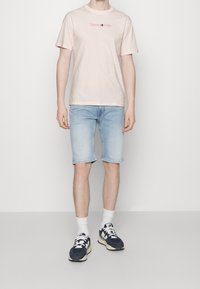 Camiseta de algodón rosa claro con el logo de "Tommy Jeans", combinada con pantalones cortos de mezclilla azul claro, calcetines blancos y zapatillas navy. Textura suave en toda la prenda.