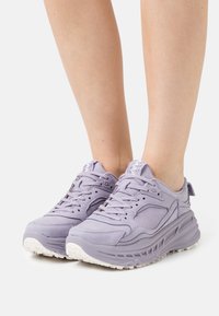 Vaaleanvioletit lenkkarit, joissa on sileä nahkapinta, teksturoidut yksityiskohdat, nauhakiinnitys ja valkoinen kumipohja, jossa on pitävät kuvioinnit.