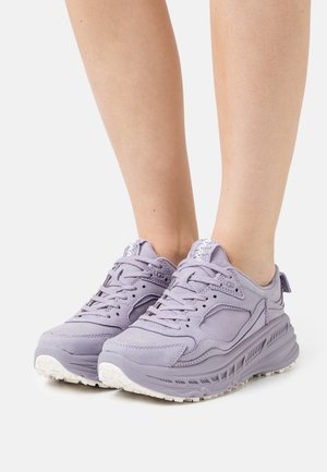Zapatillas de color púrpura claro con parte superior de piel lisa, detalles texturizados, diseño con cordones y suela de goma blanca con surcos de tracción.