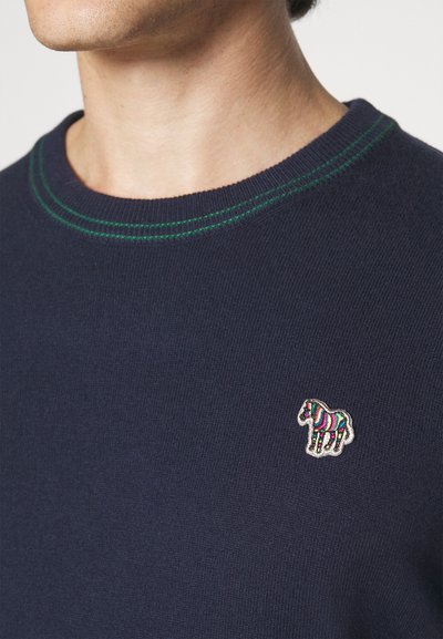 Pull marin avec un col rond, agrémenté de surpiqûres vertes et d'un patch zèbre brodé coloré sur la poitrine.