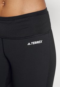 Leggings neri realizzati in tessuto elasticizzato, con una vita piatta, il logo bianco "TERREX" e dettagli di cucitura visibili.
