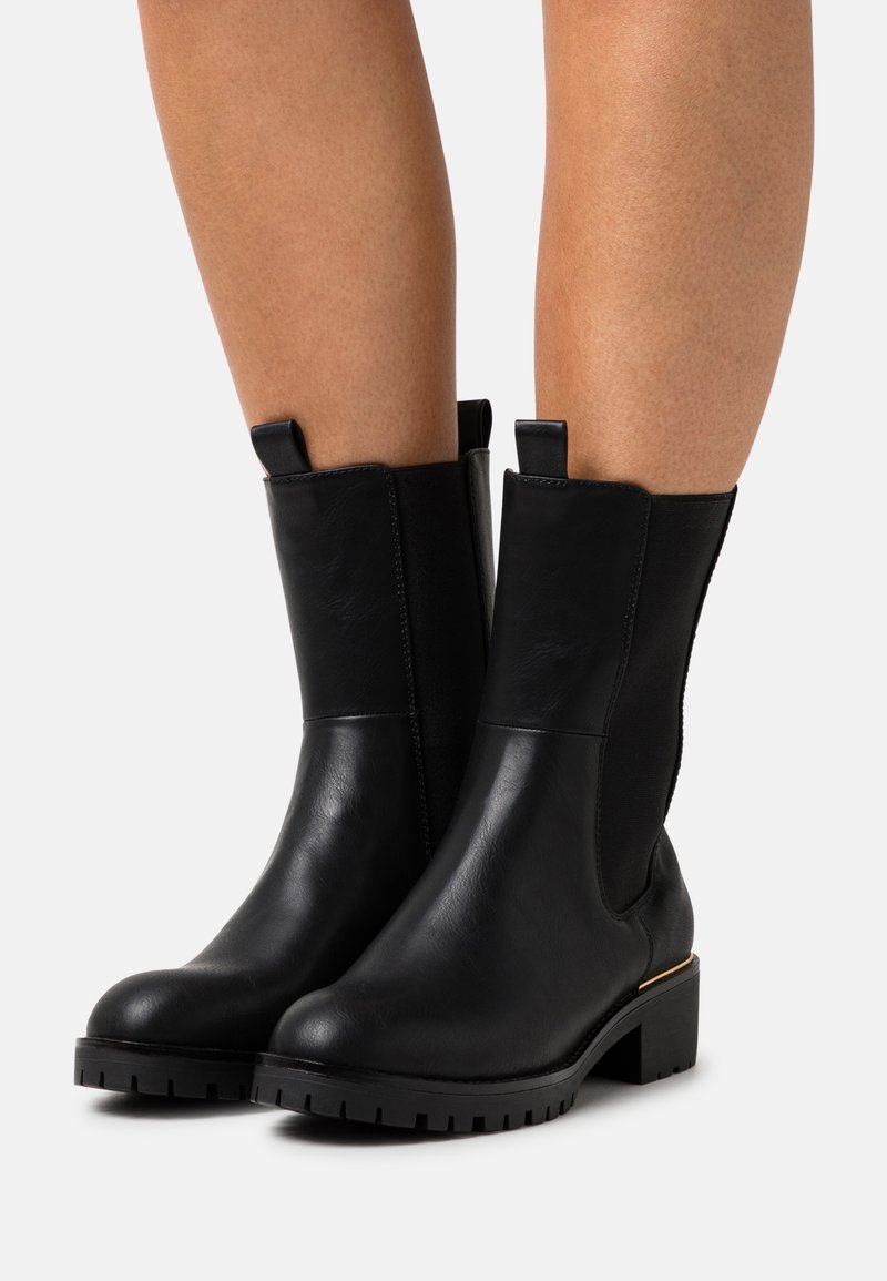Bottines en cuir noir avec des panneaux latéraux élastiques, finition texturée, semelles épaisses et un petit talon bloc avec un subtil accent doré.