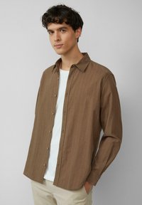 Bruine gestreepte lange mouwen shirt met een button-down kraag, met een relaxte pasvorm en een eenvoudig wit T-shirt eronder.
