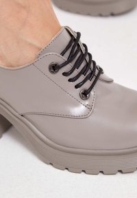 Zapatos de piel gris con cordones negros y ojales en forma de estrella. Suela de plataforma gruesa y estriada con un acabado suave.