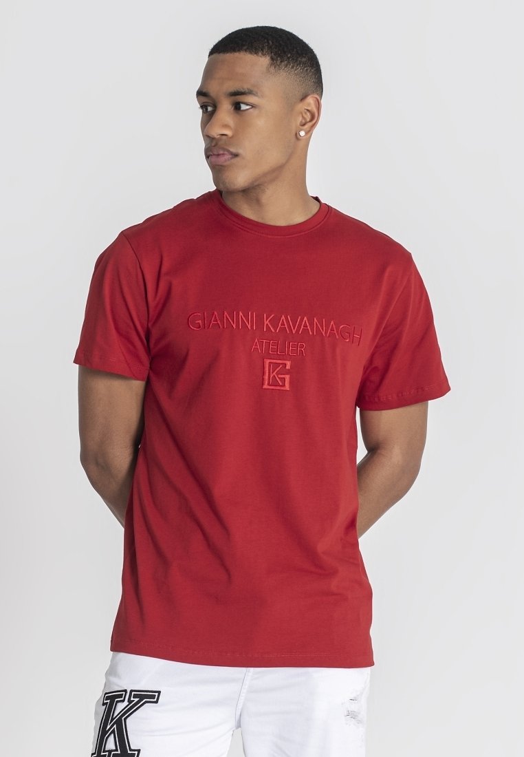 Röd bomullströja med präglad "Gianni Kavanagh Atelier"-logotyp och en fyrkantig "K"-detalj. Rund hals, korta ärmar, åtsittande design.