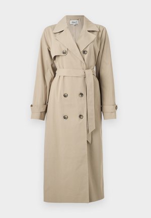 Béžový dlhý trenčkot s dvojradovým zapínaním na gombíky, širokými klopami, pásom v páse a zapínanými manžetami na jednofarebnom pozadí.