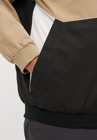 Lagana jakna s crnim, bež i bijelim panelima, elastičnim manžetama i teksturiranom završnom obradom uz detalj bočne džepne.