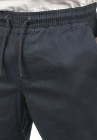 Pantalons de jogging gris foncé avec une taille élastique, cordon de serrage ajustable et une texture de tissu lisse. Présente un design minimaliste sans poches.
