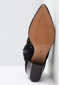 Schwarzer Wildlederschuh mit hohen Absätzen und spitzem Zehenbereich, gepunktetem Muster und brauner Gummisohle. Größe 37 ist auf der Unterseite aufgedruckt.