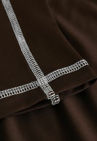 Σκούρο καφέ ύφασμα με χοντρή λευκή ραφή overlock που σχηματίζει σταυρωτό μοτίβο στην διπλωμένη άκρη.