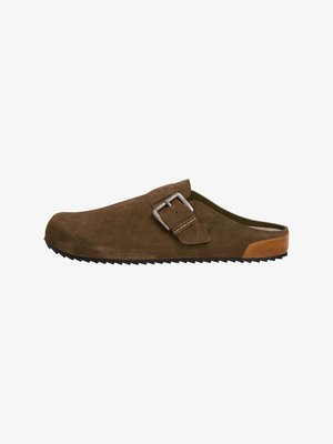 Mocassin en daim brun avec un accent en boucle en métal, semelle texturée et une finition en cuir tan au niveau du talon. Design ergonomique pour le confort.