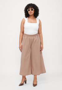 Lightweight, beige wide-leg pants with elastic waistband paired with a fitted white tank top and leopard print high heels; styled with sunglasses.