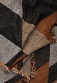 Coperta in lana con un motivo geometrico di triangoli marroni, neri e grigi. Bordo rifinito con frange per aggiungere texture e dettaglio.