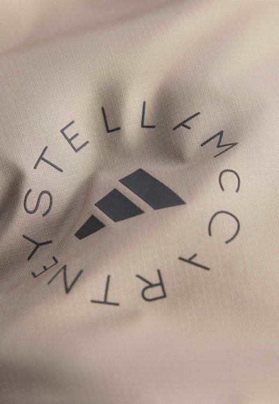 Nahaufnahme eines beigen Stoffes mit schwarzem Adidas-Logo und dem rundherum gebogenen Text "Stella McCartney".