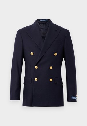 Blazer croisé bleu marine en laine, avec des boutons dorés, des revers crantés, deux poches avant et un logo discret sur le poignet.