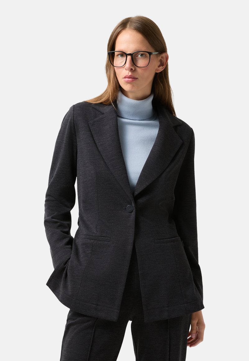 Veste taillée gris foncé avec un seul bouton, revers crantés, et deux poches avant, superposée à un pull col roulé bleu clair.