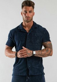 Marinblå kortärmad skjorta i mjukt, texturerat tyg med knäppning fram, inklusive en bröstficka. Har en klassisk kragdesign.