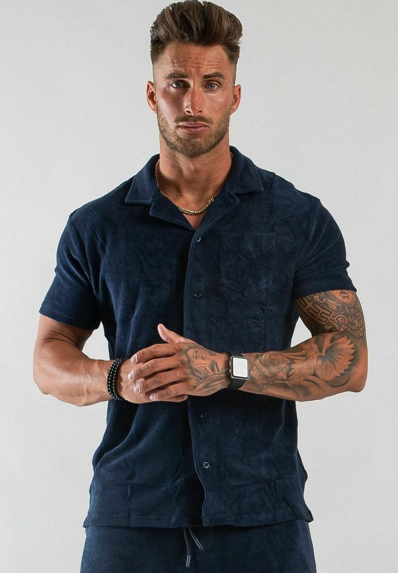 Marinblå kortärmad skjorta i mjukt, texturerat tyg med knäppning fram, inklusive en bröstficka. Har en klassisk kragdesign.