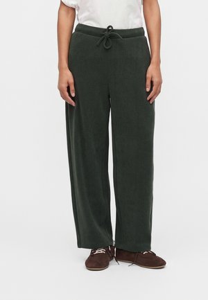 Personne portant un pantalon vert foncé à jambes larges avec taille à cordon et des chaussures marron à lacets sur fond blanc.