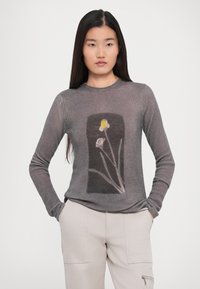 Pulover lung gri cu maneci lungi, având un design floral în alb și galben pe un fundal întunecat, realizat dintr-un țesătură texturată cu rigle.