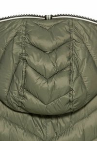 Giacca imbottita verde oliva con motivo a zigzag e cappuccio. Presenta una cerniera metallica e dettagli a righe sul tirante della cerniera.
