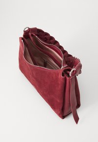 Deep red suede handbag with a braided handle, unzipped to reveal a light interior and inner pockets, set against a plain background.