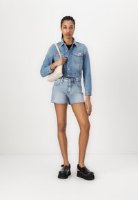 Jeans jakna u svijetloplavoj boji, sa dugmadi sprijeda i dva džepa na grudima; uparena s visokim svijetloplavim traper šortsevima i crnim platformskim cipelama.