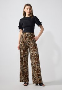 Melnas cropped blūzes ar īsām piedurknēm, kas apvienota ar platajām biksēm ar brūnu un melnu leoaprdzīvojumu. Modelis valkā melnas sandales ar atvērtu purngalu.