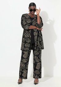 Mustat kukkakuosiset puvut, jotka on valmistettu teksturoidusta kankaasta, sisältävät pitkän takin ja leveät housut, yhdistettynä teräväkärkisiin korkokenkiin ja aurinkolaseihin.