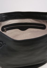 Czarna skórzana torba na ramię o gładkiej fakturze z wewnętrzną kieszenią na zamek. Podszewka to beżowy materiał z minimalistycznym wzorem.