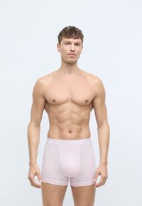 Gaiši rozā bokseršorti ar mīkstu tekstūru un ciešu piegulumu. Iekļauta logotipa josta un gluda priekšējā paneļa. Modelis pozē pašpārliecināti.