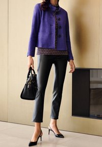 Chaqueta de lana morada con botones negros, blusa estampada, pantalones de cuero sintético negros y bolso negro; lleva puestos tacones de salón negros.