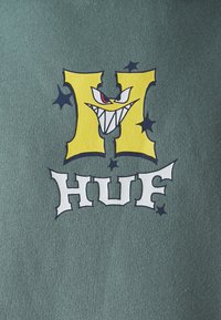 Zöld szövet, amelyen egy nagy sárga "H" látható fogakkal rendelkező arccal, valamint a fehérben stilizált "HUF" felirat. Kicsi fekete csillagokkal érzékeltetve.