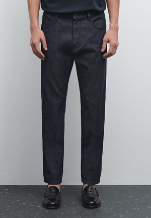 Dark blue denim jeans with a straight fit, featuring front pockets and a button closure. Smooth texture with minimal stitching details.