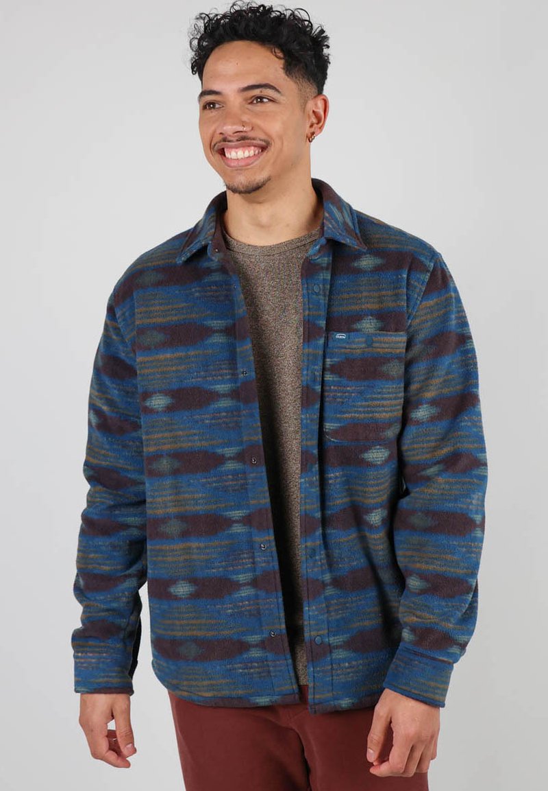 Chemise en flanelle avec des motifs abstraits bleu, vert et marron. Présente un devant à boutons et une poche poitrine. Texture douce avec une coupe décontractée.