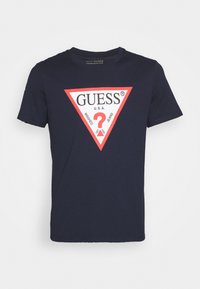 T-shirt in cotone blu navy con un design a logo triangolare rosso con la scritta "GUESS U.S.A." e un punto interrogativo al centro. Maniche corte.
