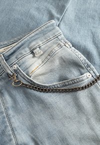 Lichtblauwe denim jeans met een kettingdetail op de voorzak, voorzien van subtiele vervaging en stiksels. Knoopsluiting bij de tailleband.