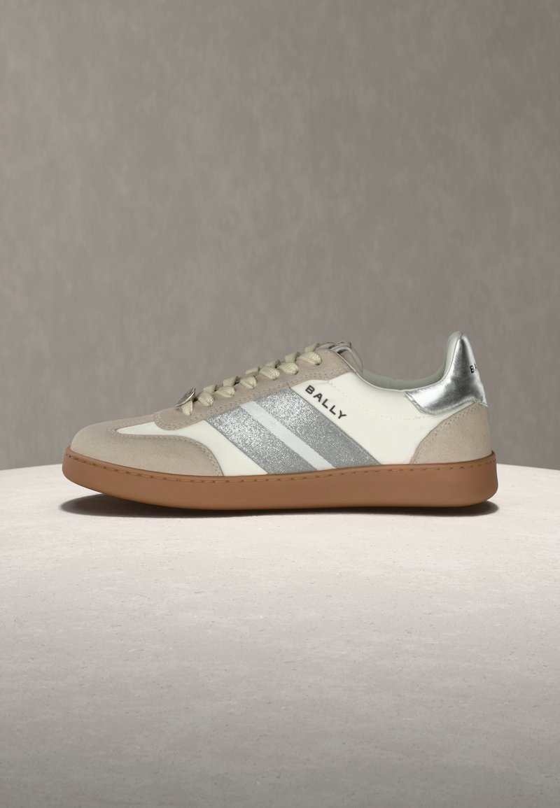 Baskets basses en daim beige, côtés rayés blancs et argentés, languette de talon argentée, logo "BALLY" et semelle en caoutchouc gomme sur un fond neutre.