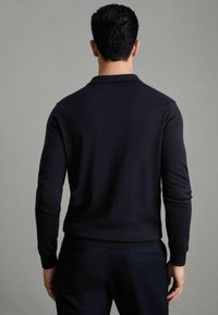 Polo din material moale, cu mânecă lungă, de culoare bleumarin, cu guler și manșete ribificate, având un design ajustat și o textură netedă.