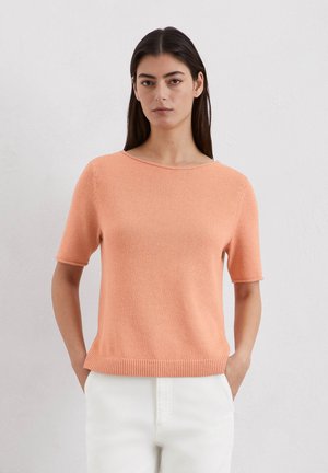 Kurzarmpullover in Pfirsichfarbe aus Strickstoff, mit weitem Ausschnitt, geripptem Saum und subtiler Textur. Kombiniert mit hellen Hosen.